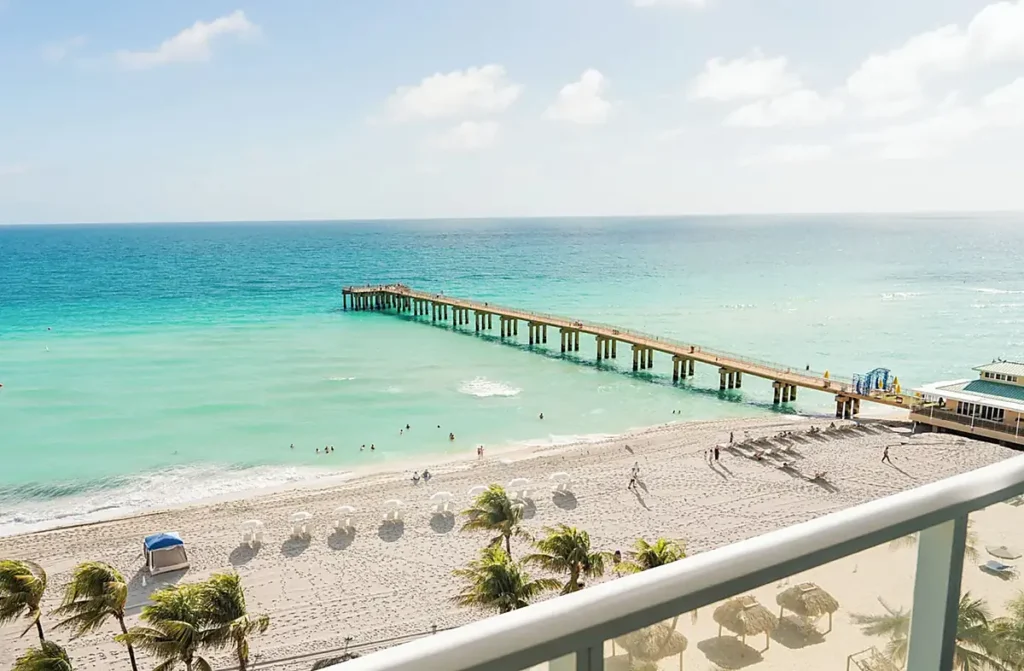 Vista do The Sunny Miami para o mar azul-turquesa, a praia de areia branca e o píer de Sunny Isles Beach, na Flórida.