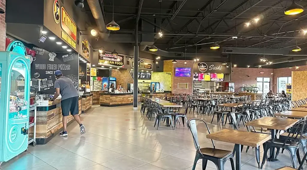 Área de alimentação do Lake Buena Vista Factory Stores, com restaurantes, mesas ao ar livre e vista para o lago com fonte.